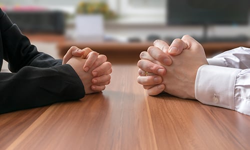 Two sets of hands clasped together siting across a table